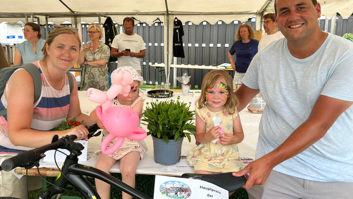 Volltreffer bei der Tombola! Die stolze Gewinnerin präsentiert das soeben gewonnene neue Fahrrad im Kreis ihrer Familie.