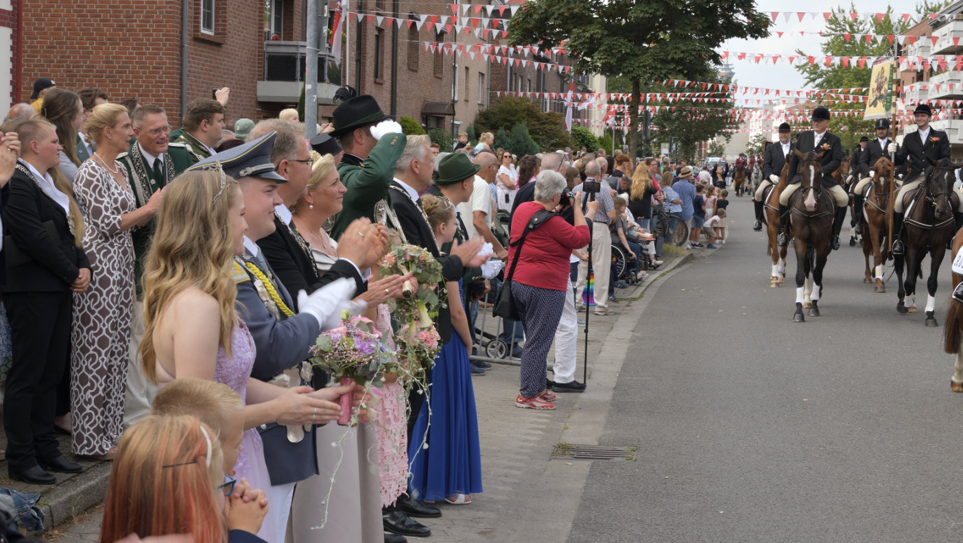 Königspaare, Chefs, Präses und Ehren­gäste zollen den vorbei­ziehenden Schützen nebst Reitern während der Parade immer wieder Applaus.